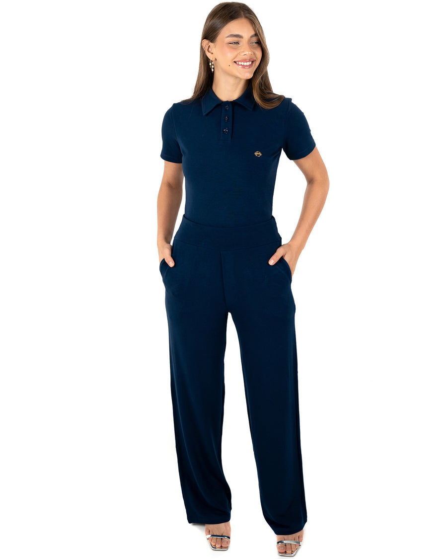 Scrub feminino Ivy moletinho azul marinho de frente, mãos nos bolsos da calça pantalona e blusa gola polo
