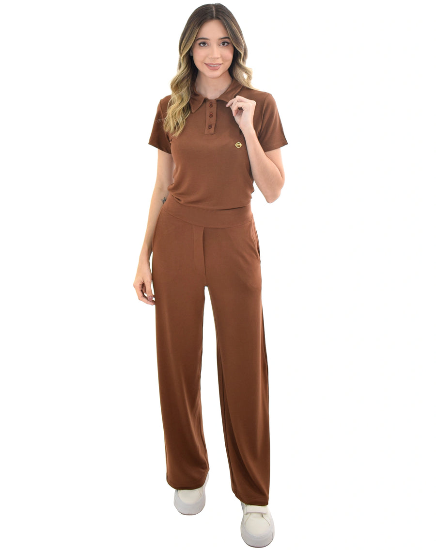 Scrub feminino Ivy moletinho marrom, modelo segurando a gola polo com botões, calça pantalona com bolsos