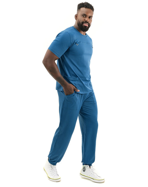 Scrub masculino Neo Soft azul petróleo de lado, modelo com mão no bolso e calça jogger com punho elástico