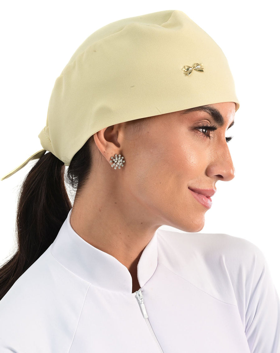Touca bandana feminina amarelo creme em modelo, vista lateral com lacinho dourado aplicado e amarração atrás