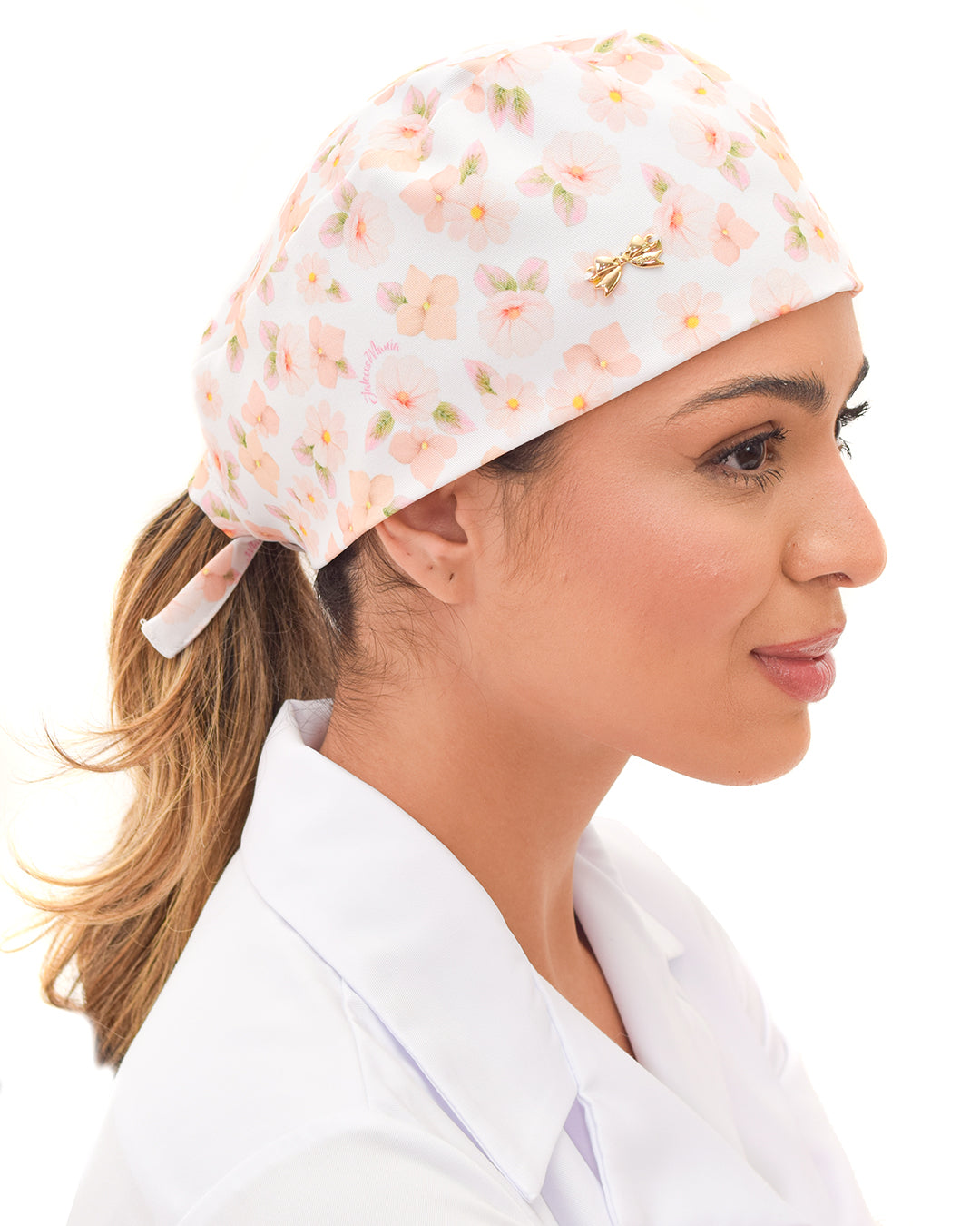 Touca bandana feminina Gardênia em modelo, vista lateral, fundo branco com estampa floral em tons pastel e lacinho dourado