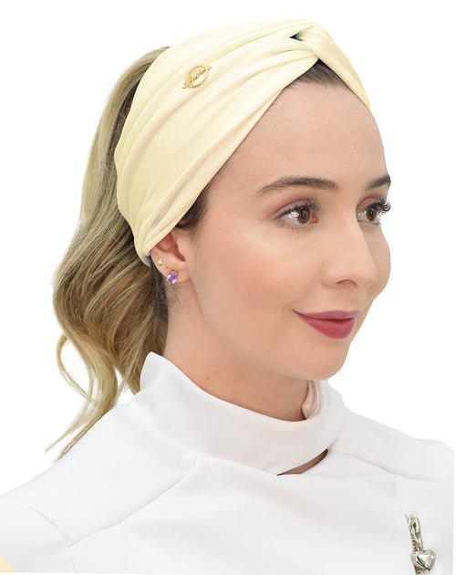 Turbante feminino amarelo creme em modelo, vista lateral, com franzido torcido na frente e pin dourado da marca