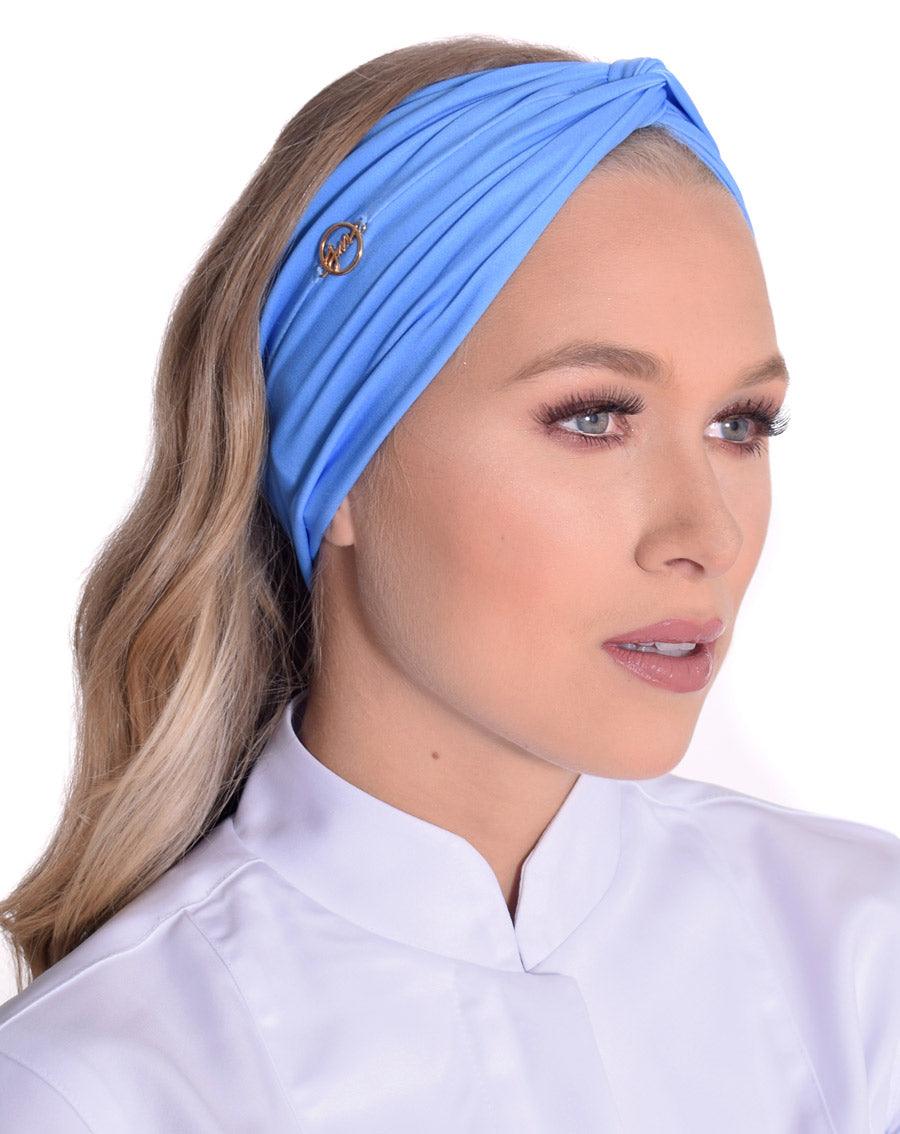 Turbante feminino azul serenity em modelo, vista frontal, com tecido cruzado no alto e pin dourado da marca