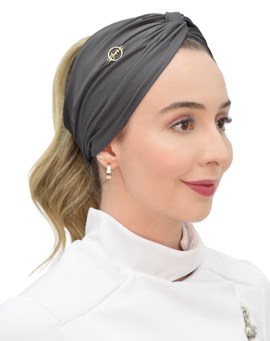 Turbante feminino cinza chumbo em modelo, vista lateral, com nó torcido no alto e pin dourado da marca