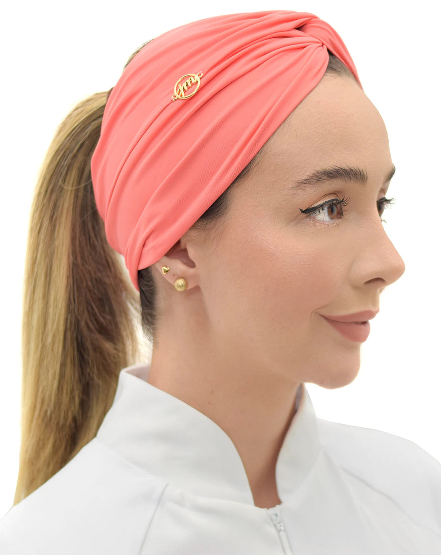 Turbante feminino goiaba em modelo, vista lateral, com nó torcido no alto, pin dourado e cabelo preso em rabo
