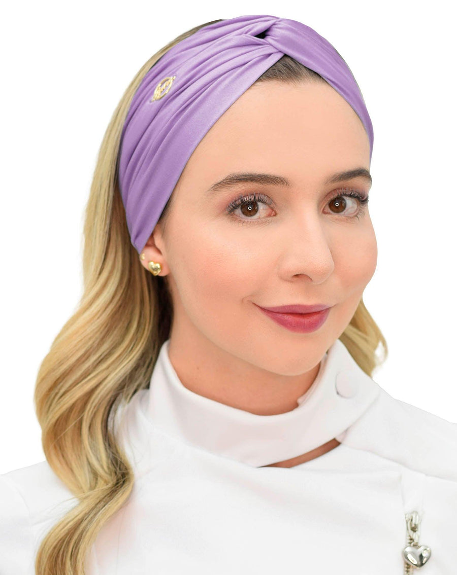 Turbante feminino lavanda em modelo, vista frontal, tecido acetinado lilás com nó torcido e pin dourado