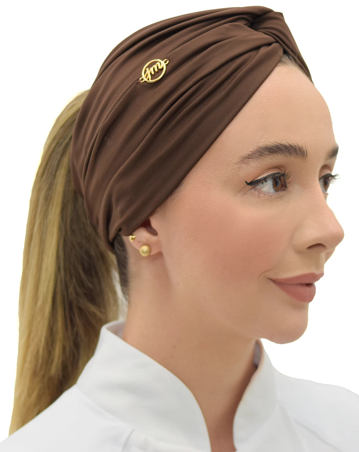 Turbante feminino marrom em modelo de perfil com rabo de cavalo, tecido drapeado e logo dourado da marca — foto 2