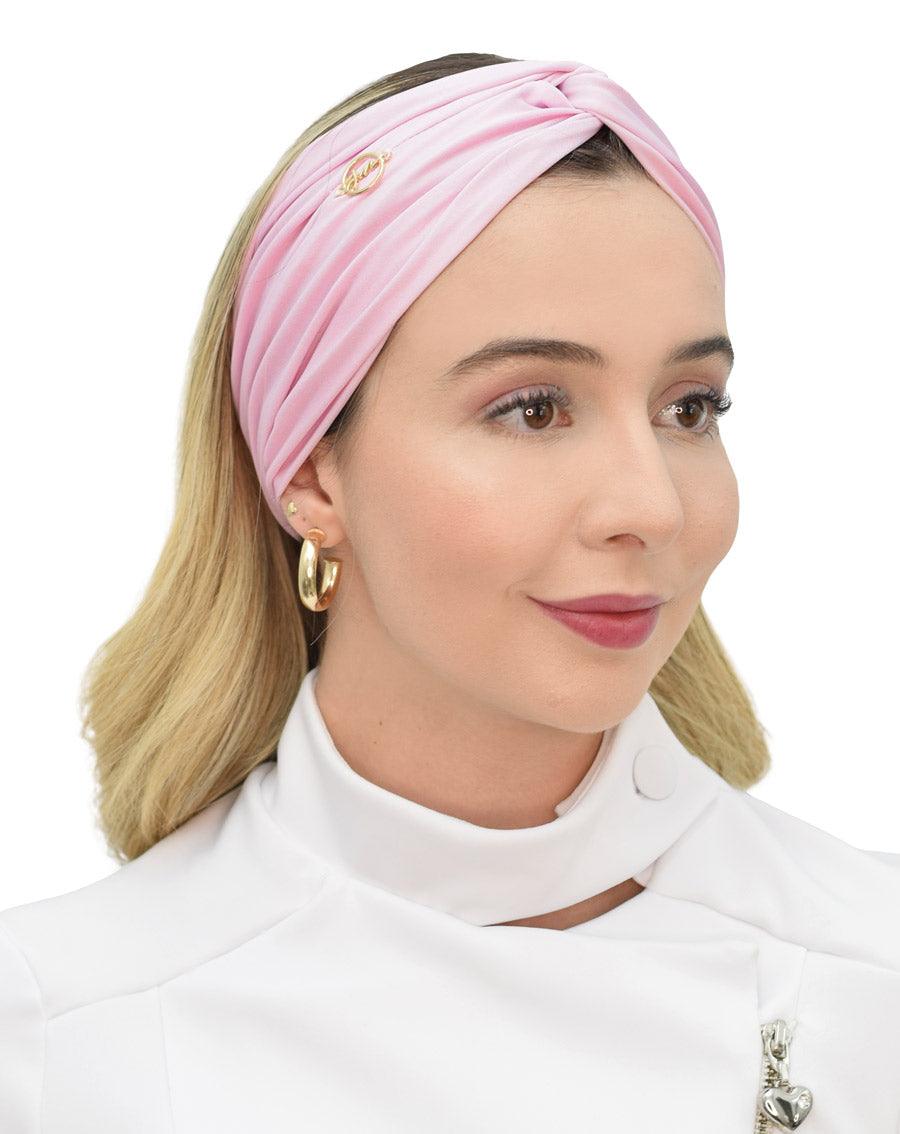 Turbante feminino rosa claro em modelo, vista frontal, nó torcido no topo, tecido franzido e pin dourado