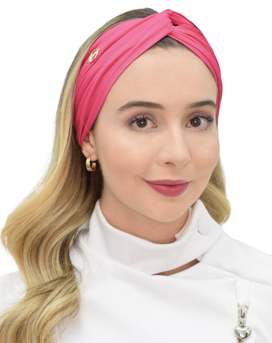 Turbante feminino rosa pink em modelo, vista frontal, nó torcido no topo e tecido franzido com logo dourado — foto 2