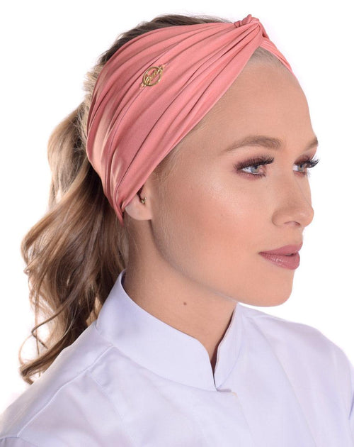 Vista lateral do turbante feminino rosé em modelo, destacando o franzido do tecido e o detalhe dourado da marca
