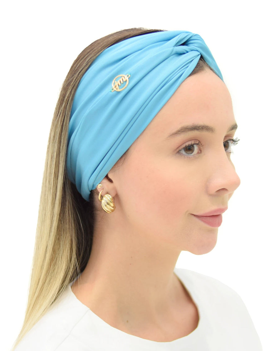 Vista lateral do turbante feminino turquesa em modelo de cabelo solto, mostrando drapeado do tecido e pin dourado