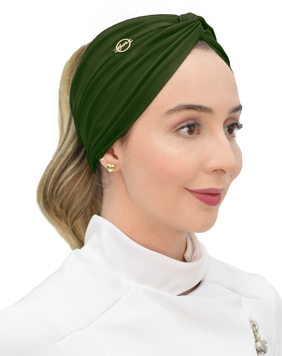 Modelo de rabo de cavalo usando turbante feminino verde militar com nó torcido e emblema dourado, sobre jaleco branco