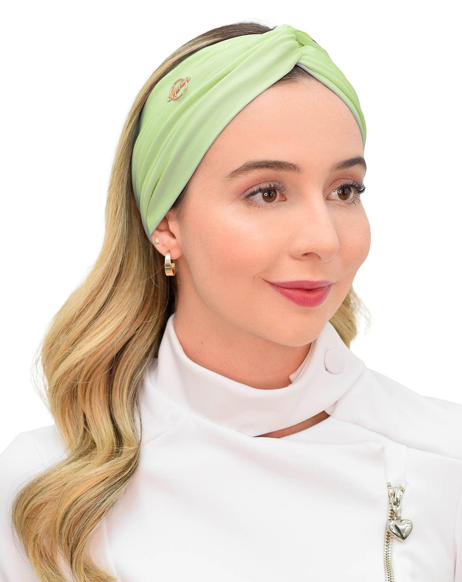Vista frontal do turbante feminino verde pistache em modelo de cabelo solto, com trançado torcido e pin dourado