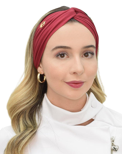 Vista frontal do turbante feminino vinho bordô em modelo de cabelo solto, com drapeado do tecido e pin dourado